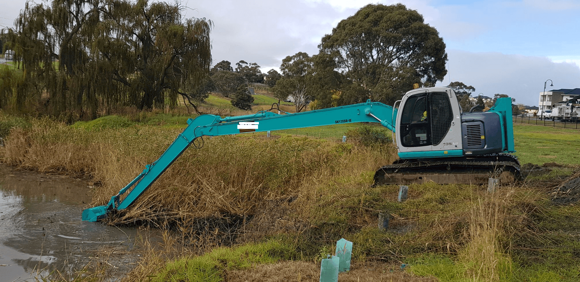 Excavator clearing vegetation along a creek bank